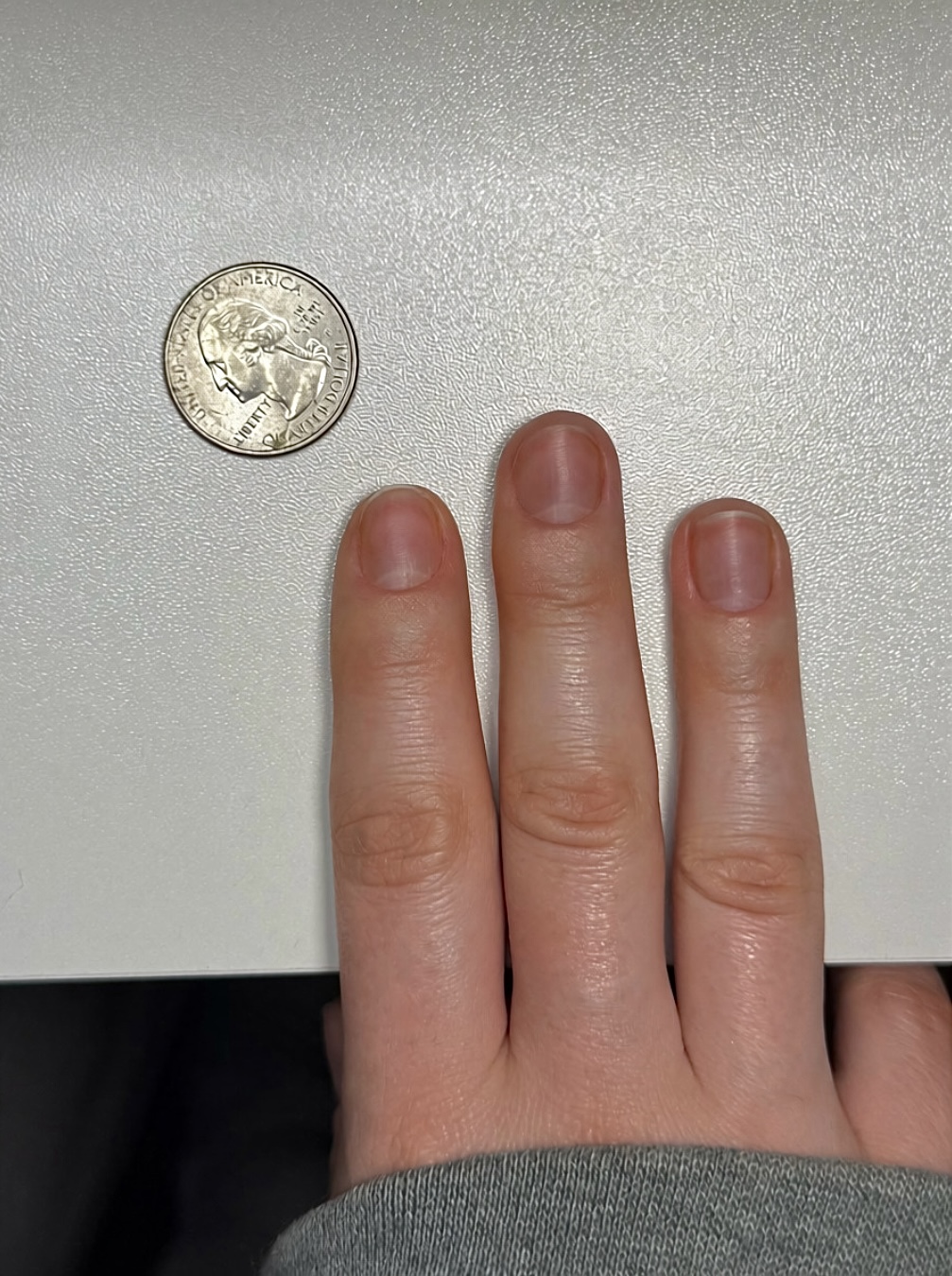 Example sizing photo showing index, middle, and ring nails beside a quarter